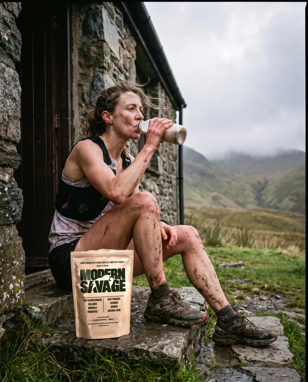 A runner sitting on a cottage step after a muddy run, drinking milk, a Modern Savage pouch beside her
